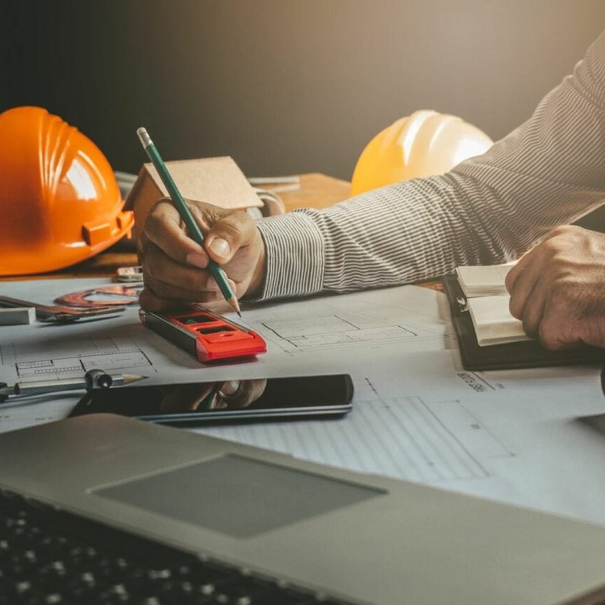 close up shot of an engineer's hand holding a pencil with engineering helmets in the background