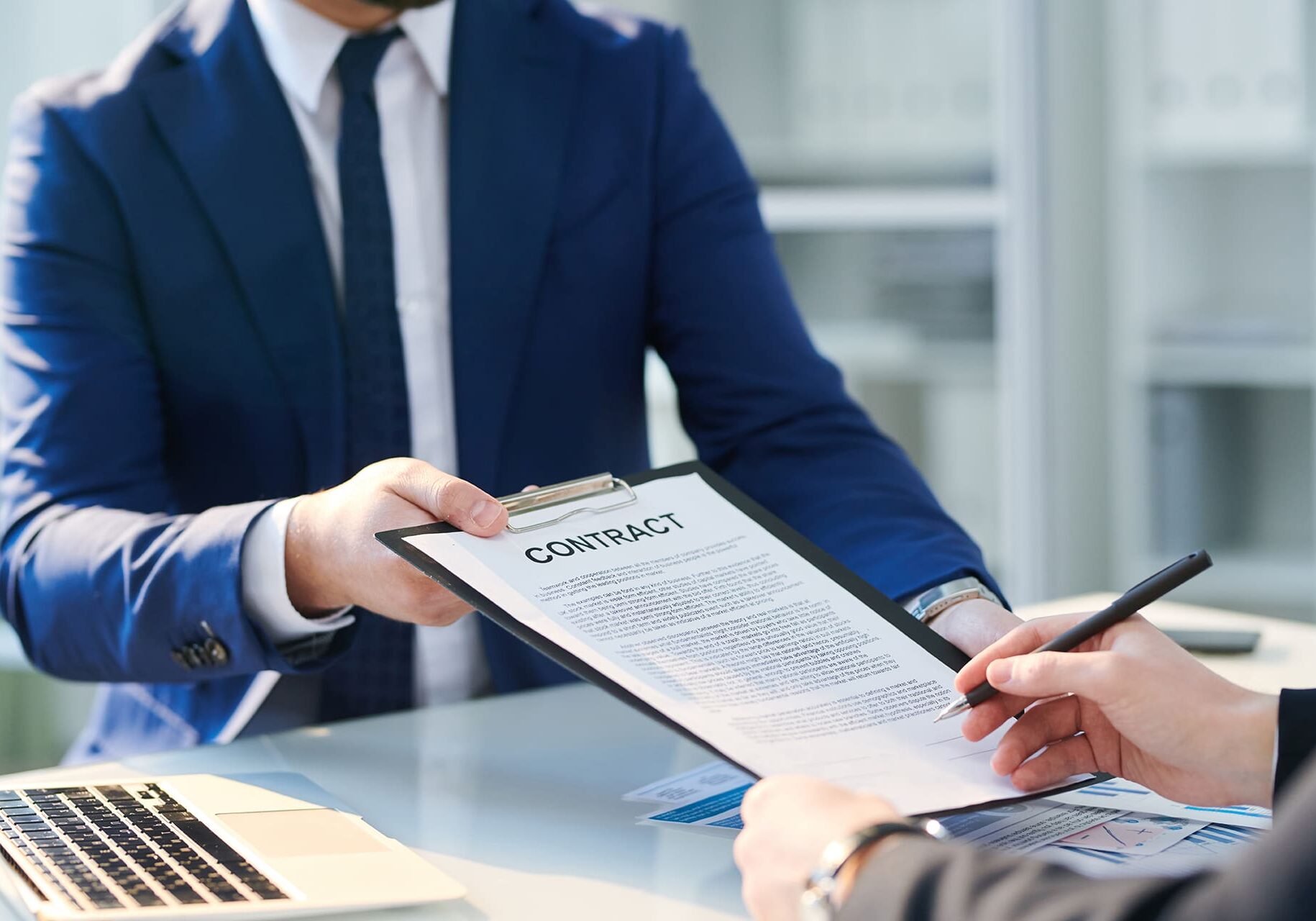 One of young successful businessmen signing contract held by the other after negotiation in office